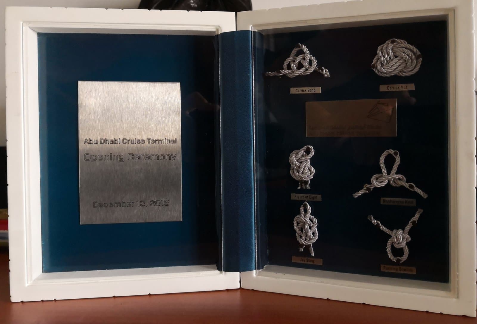 Open book-style display with a blue-framed inscription panel and small emblems on a dark opposite page