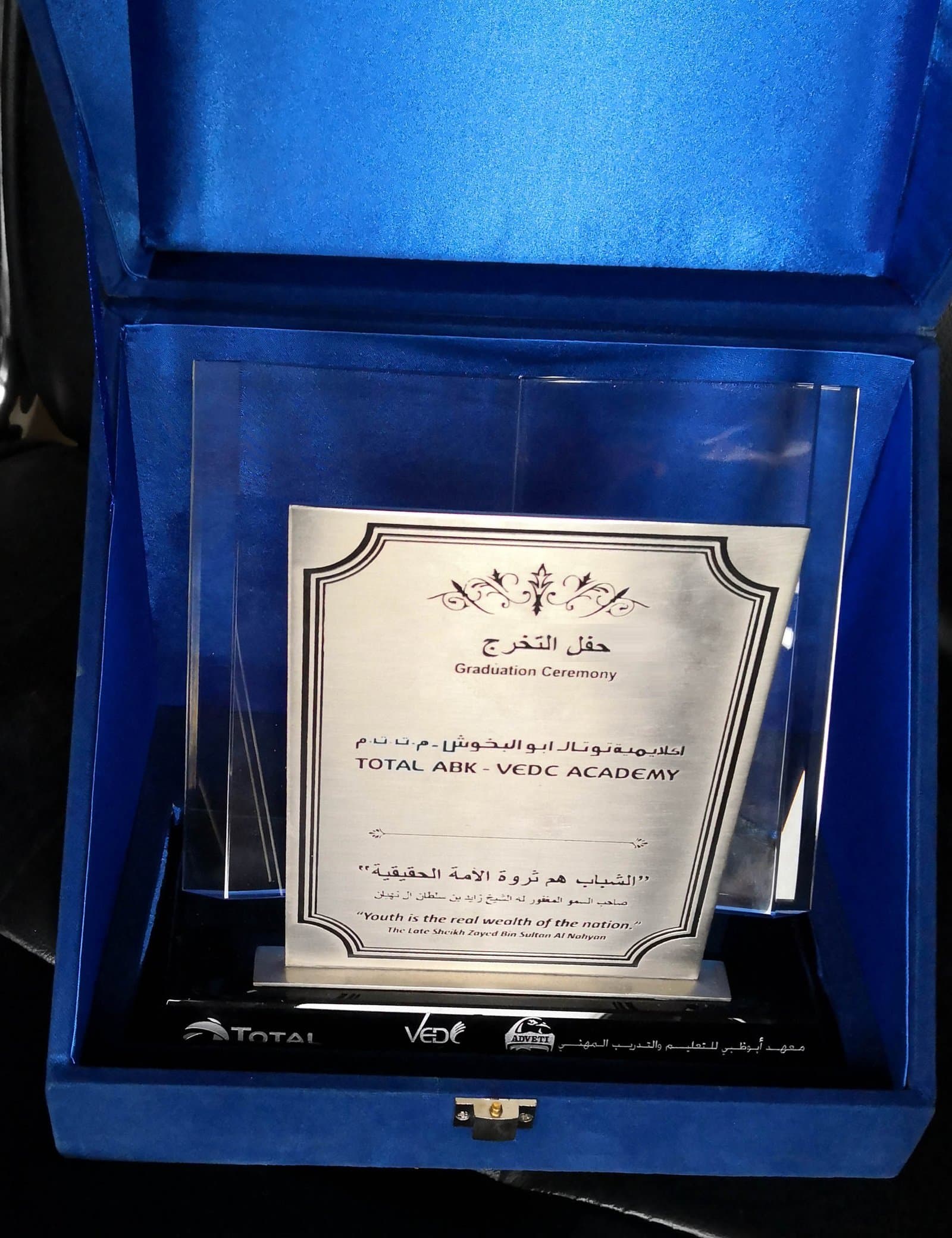 Framed silver-toned dedication plaque on a dark foot inside an open blue presentation case