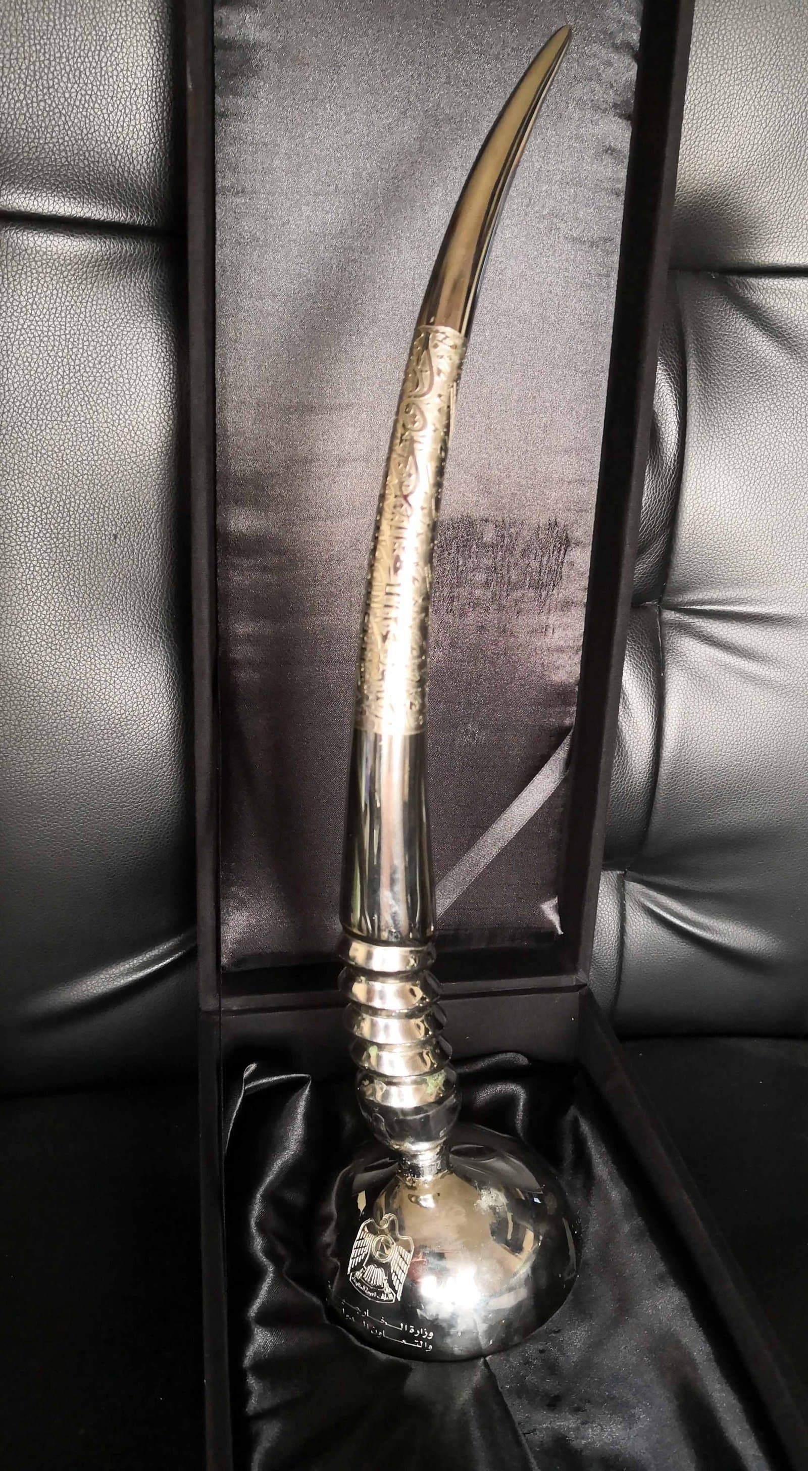 Tall sword-shaped metal trophy with a curved blade-like form and an ornate hilt