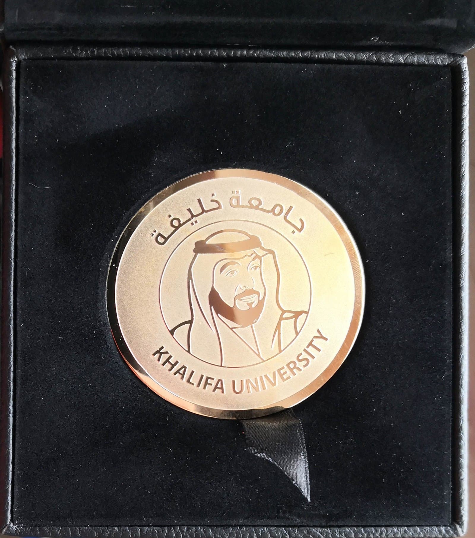 Round gold-toned portrait and emblem medal centred in a dark square presentation panel