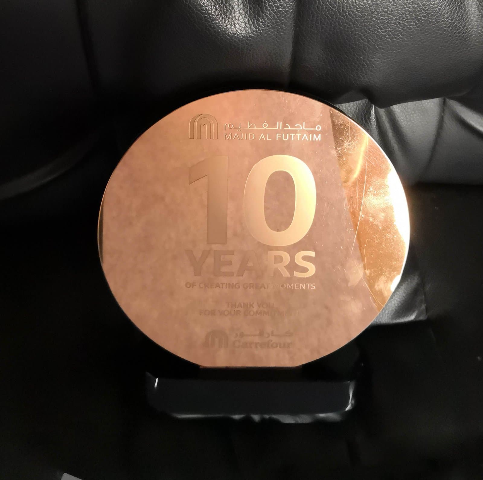 Reflective warm-toned circular anniversary award with a subtly faceted edge and dark display foot