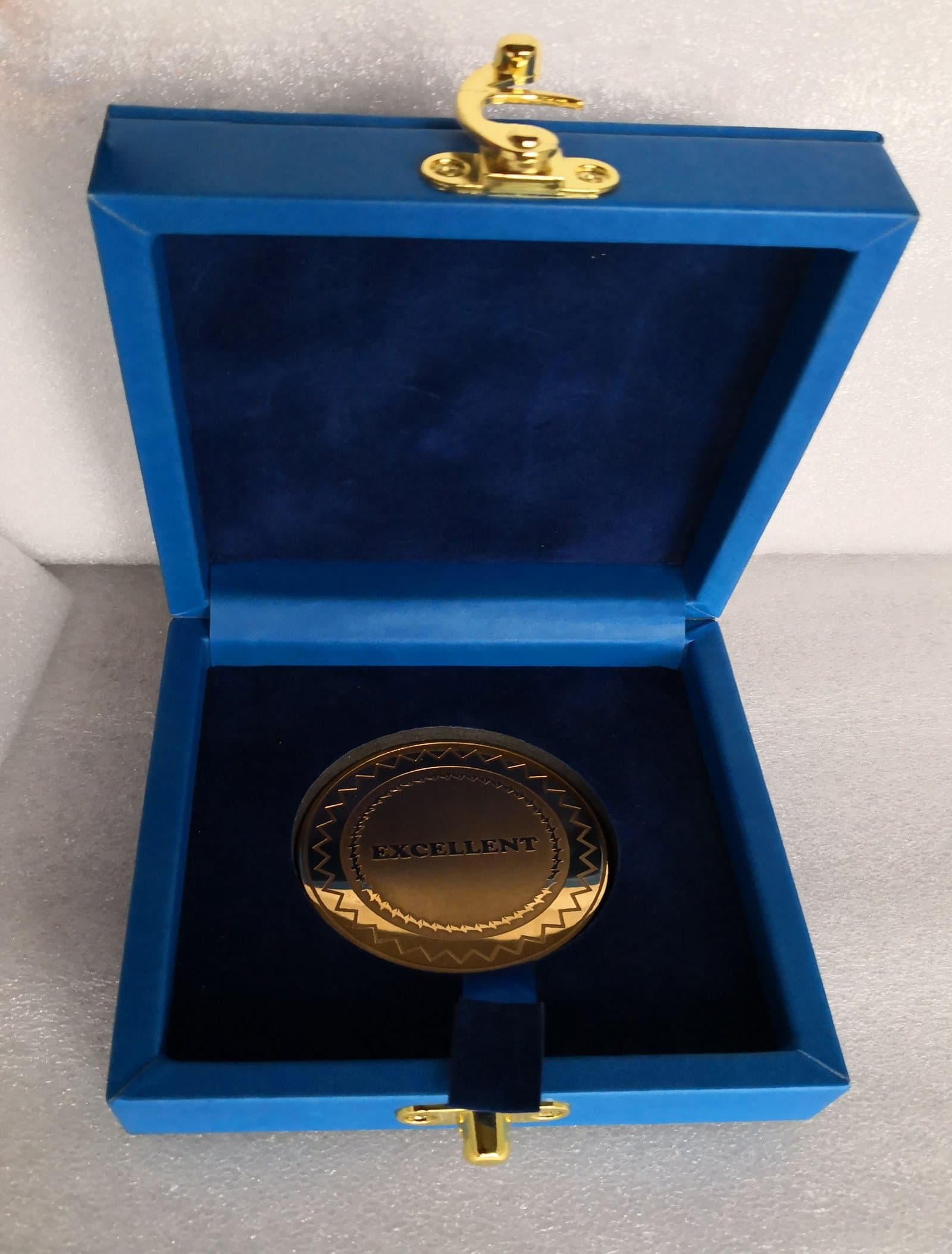 Gold-toned circular medal inside an open blue lined presentation case