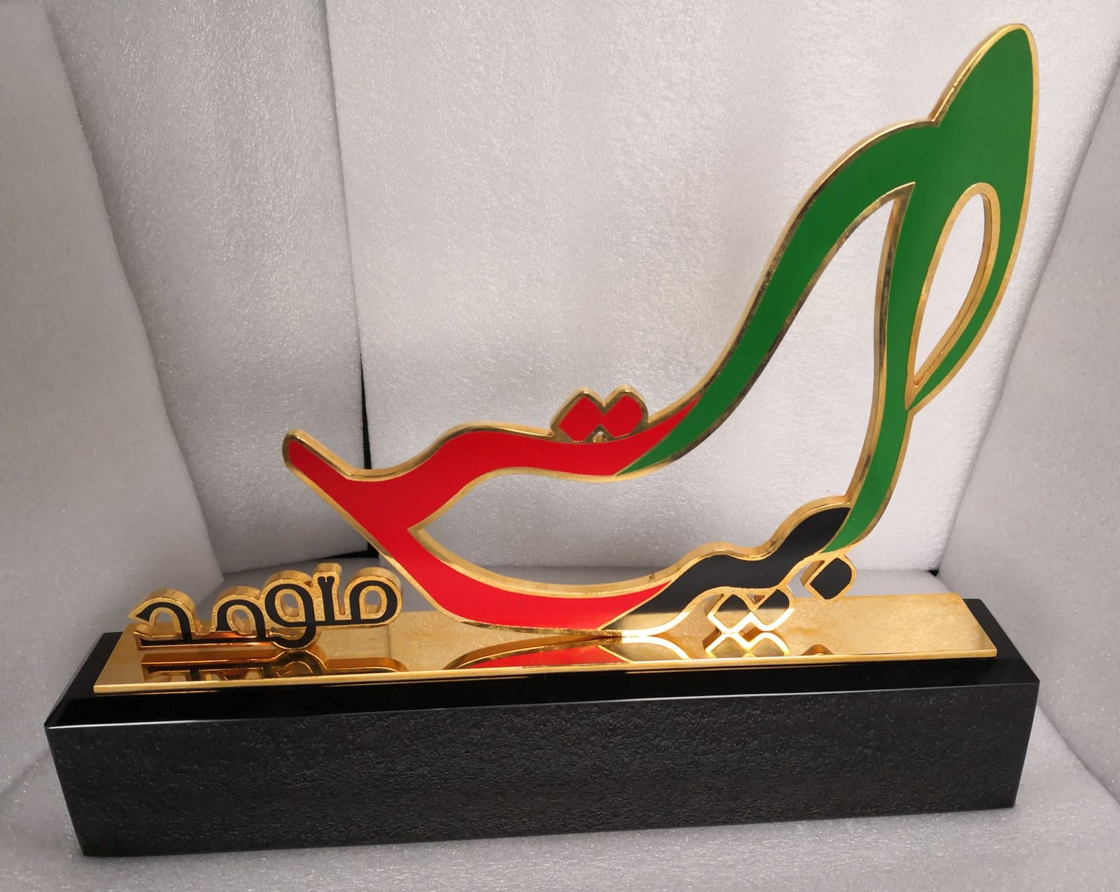 Red and green sweeping calligraphic metal form with gold-toned edges on a black base