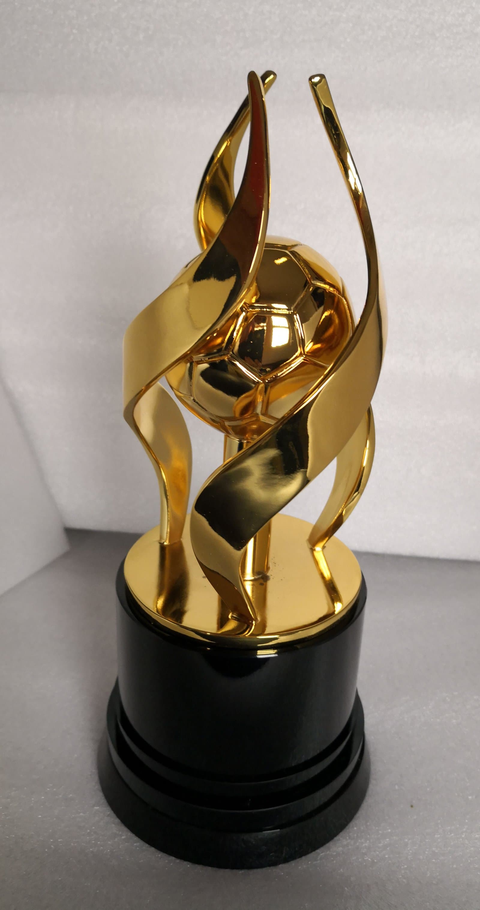 Gold-toned sports trophy with twisting upright ribbons and a round centre on a stepped dark foot