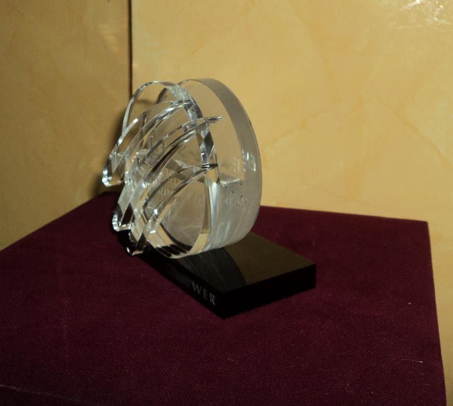 Layered clear circular award with overlapping curved elements on a dark rectangular base