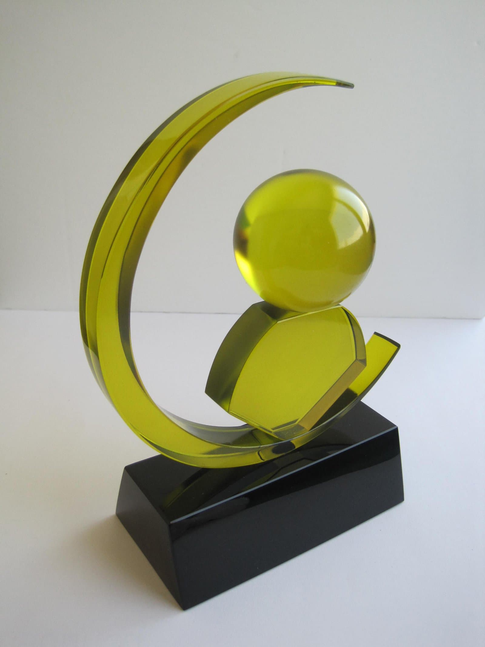 Yellow crescent-shaped award surrounding round and faceted yellow forms on a black base