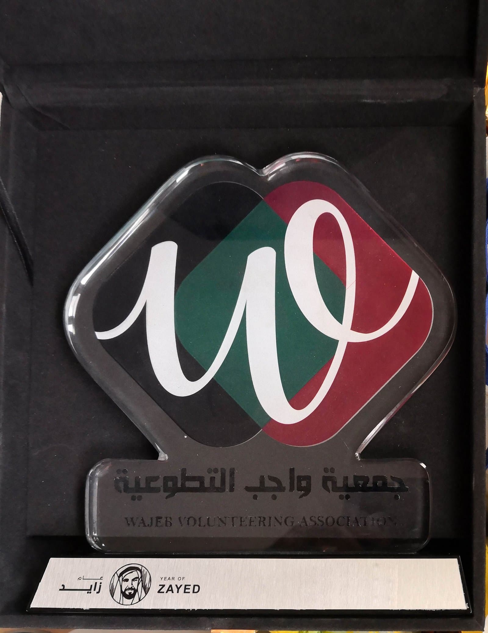 Diamond-shaped award with white calligraphic strokes, red and green areas and a dark presentation case