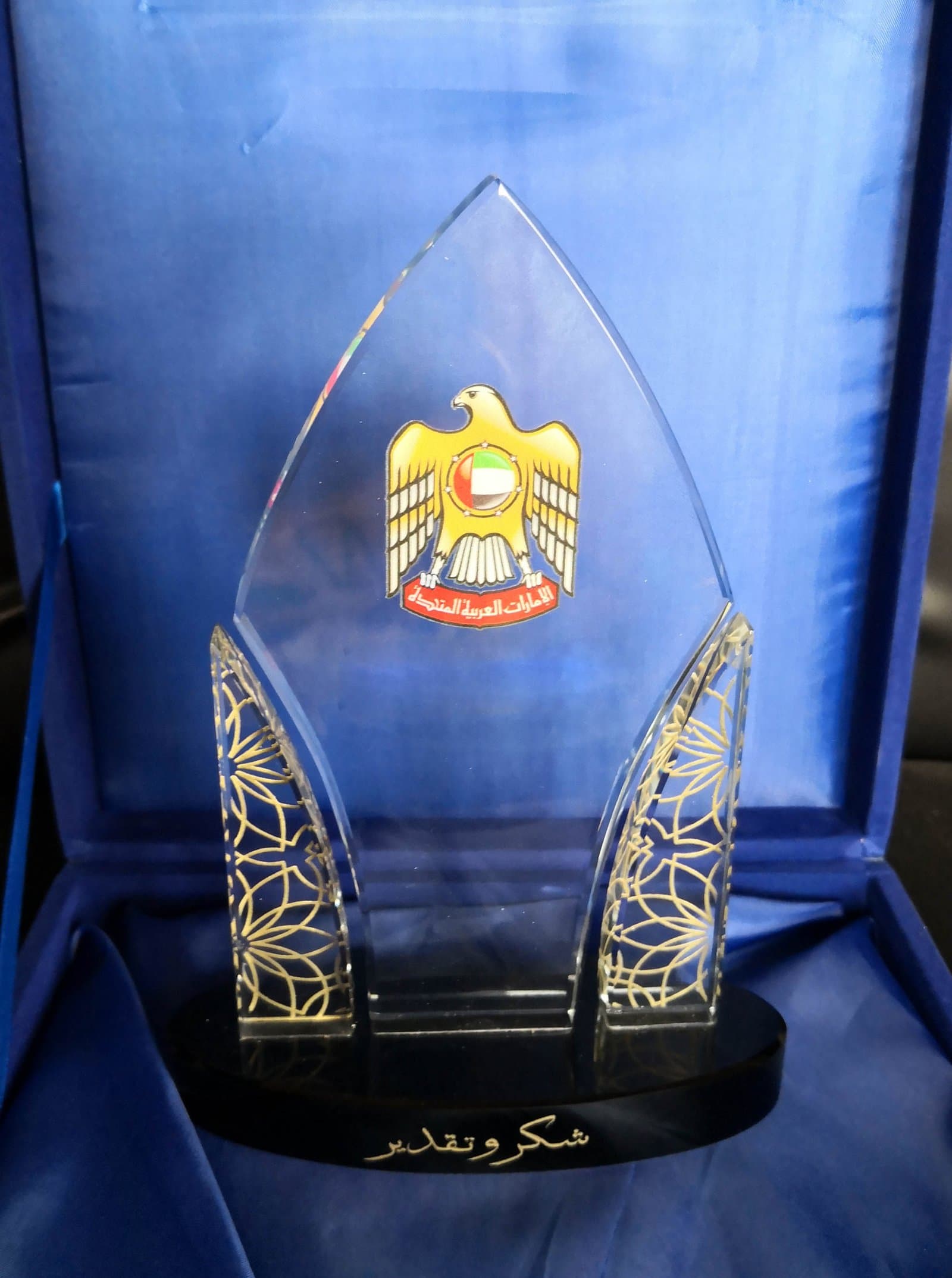Pointed clear award with a UAE emblem, patterned side elements and a dark base inside a blue case