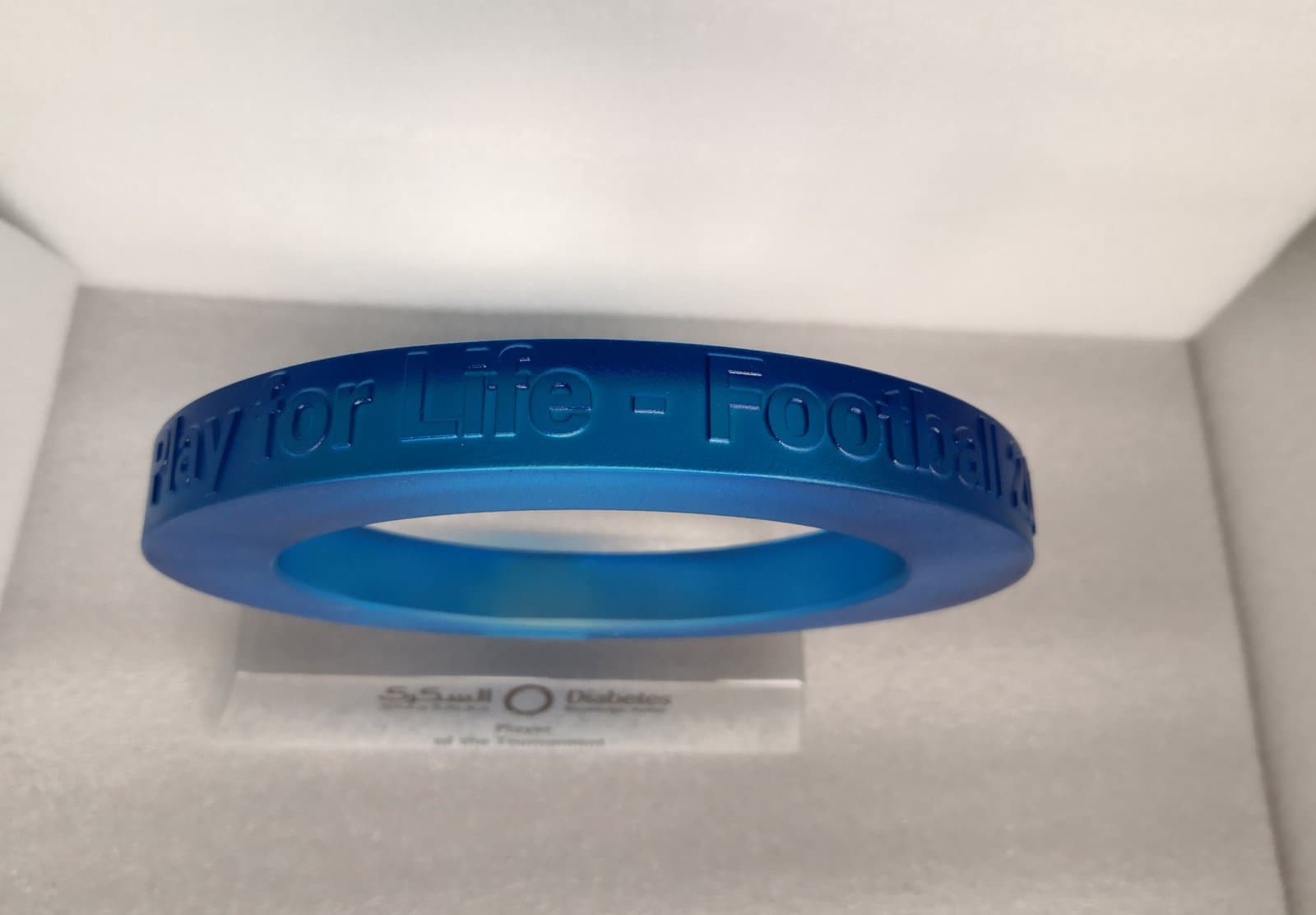 Blue circular band with lettering shown inside a pale presentation interior
