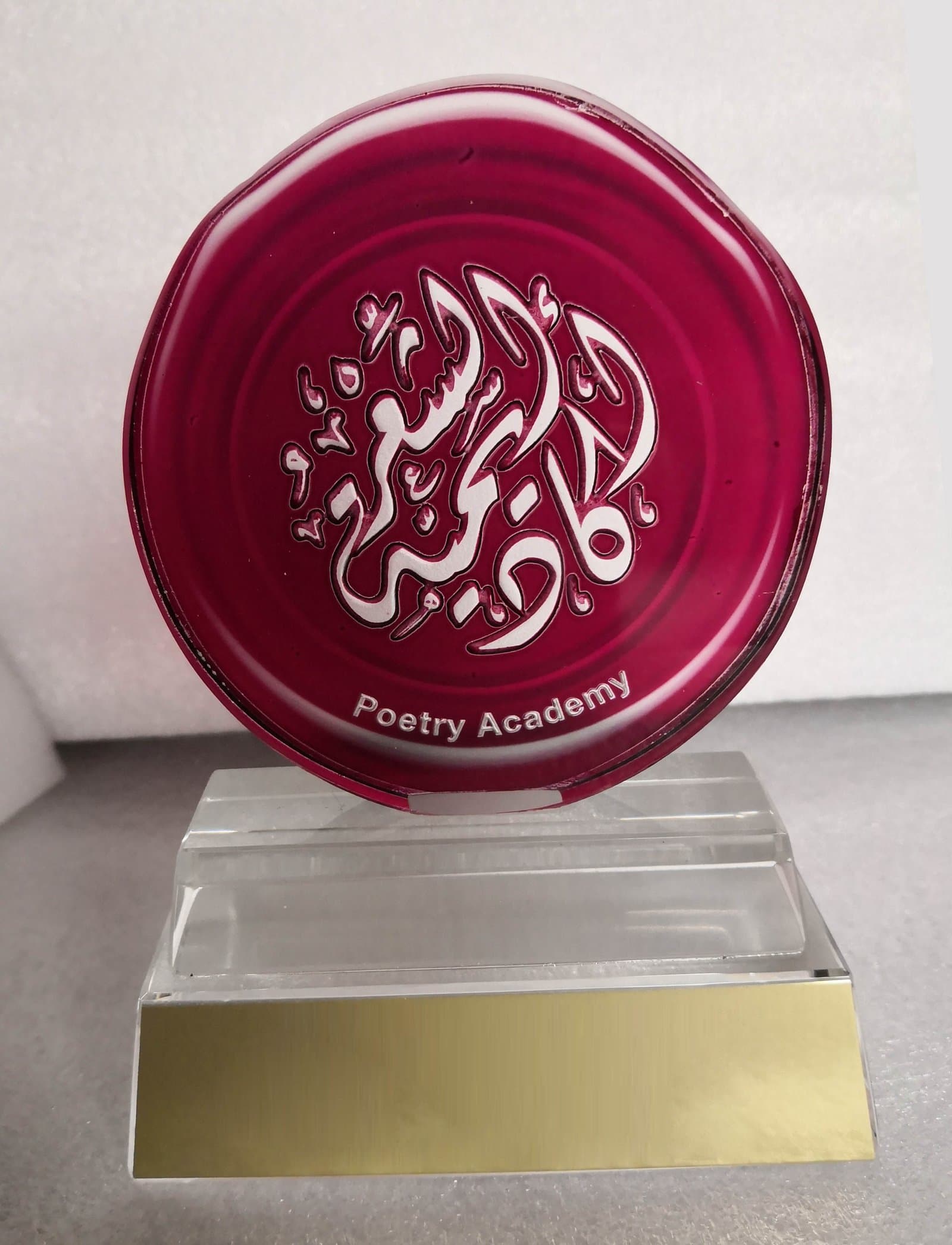 Deep red circular award with white Arabic calligraphy on a clear stepped support