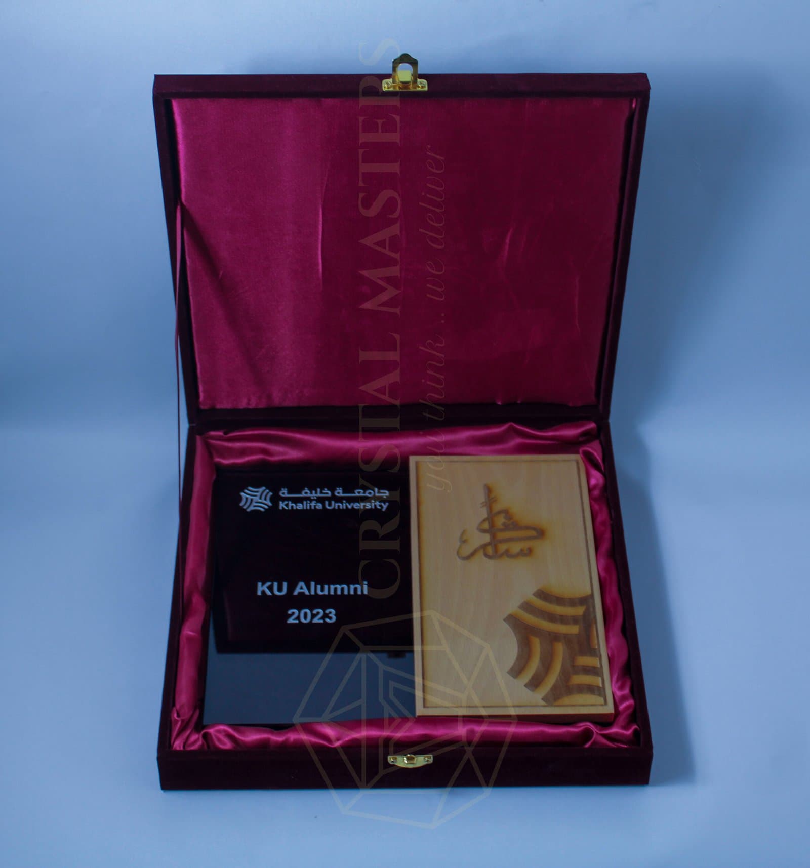 Open maroon lined case holding a dark inscription panel and a lighter gold-emblem presentation piece
