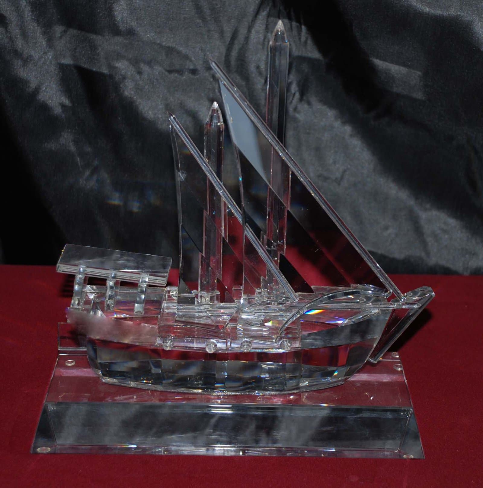 Transparent dhow miniature with upright masts, angular sails and red hull accents on a clear base
