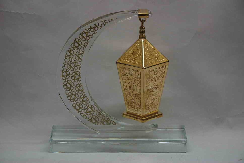 Patterned crescent surrounding a hanging gold-toned lantern on a clear rectangular base