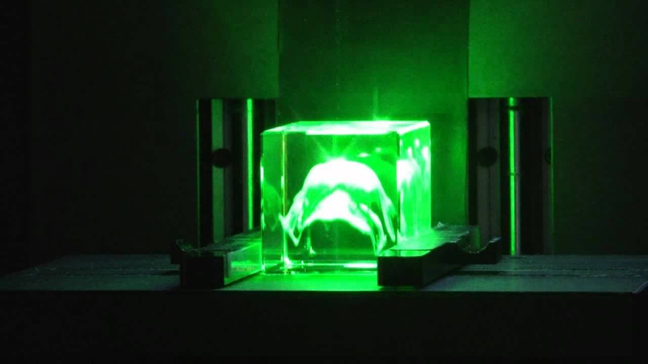 Green-lit crystal block with a horse image between dark engraving-machine components